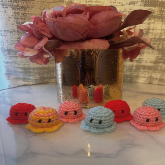 Seven tiny crochet octopuses with smiling faces in red, yellow, pink and blue
