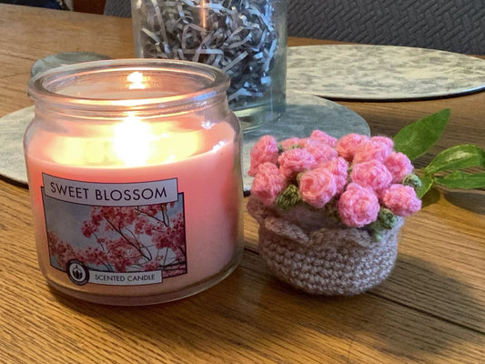 A crochet pot of pink roses beside a lit candle